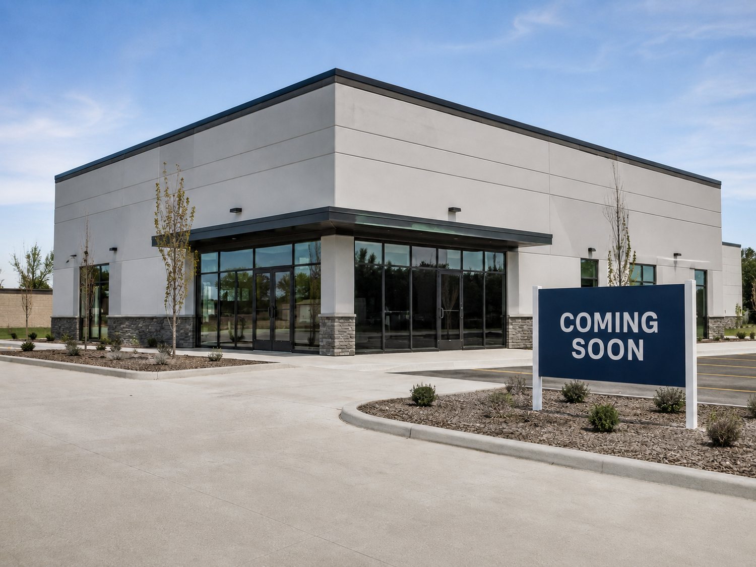 Newly completed single-story commercial retail building with storefront glazing and a coming soon sign in the parking lot